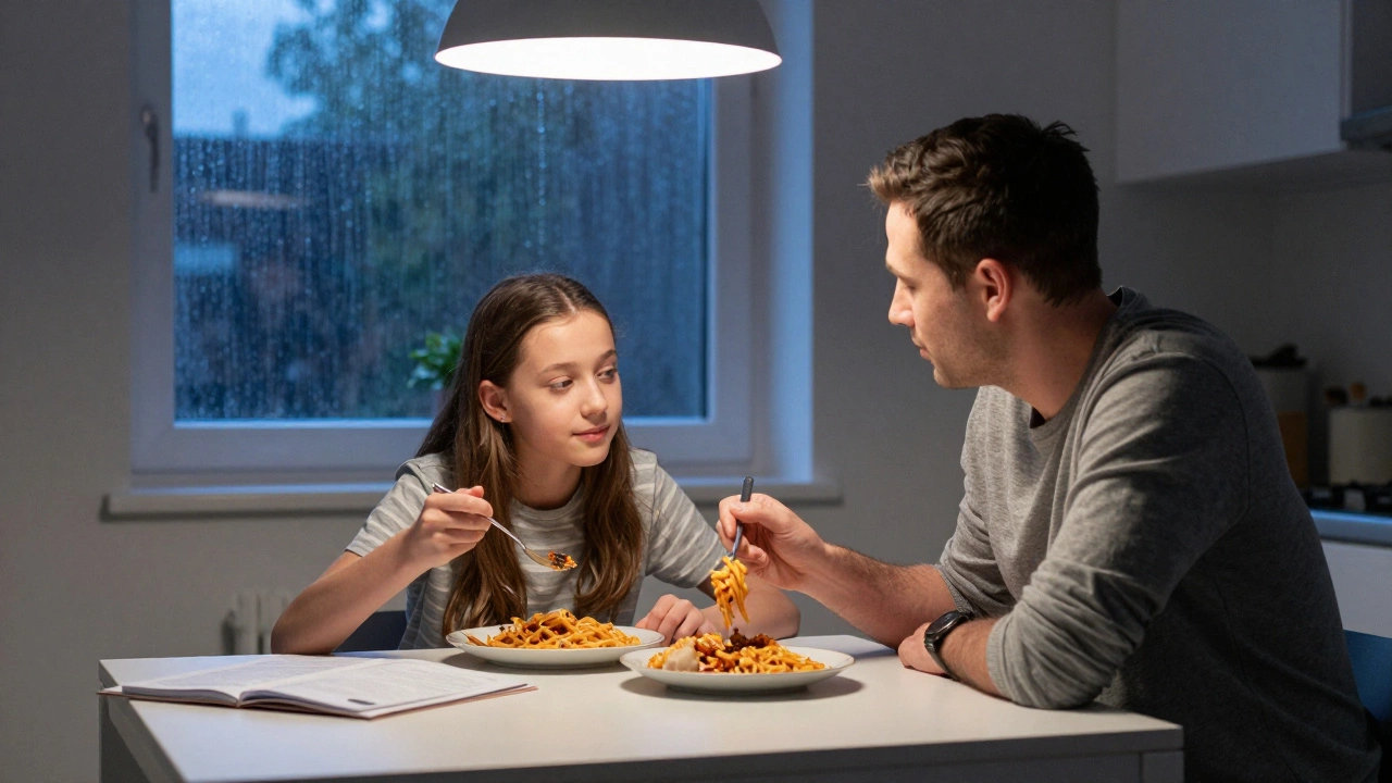 Father and daughter eating microwave pasta together at night, debate folder beside them, rain on the window behind.